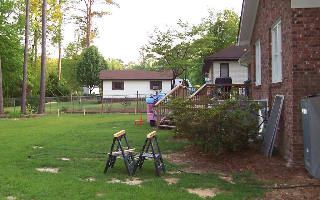 Before: a plain backyard with patchy lawn and bare ground along the house