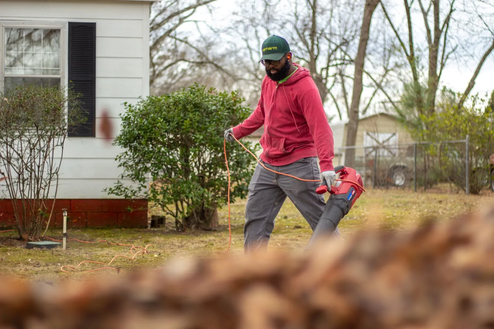 Worker clearing a deep pile of fallen leaves beside a house