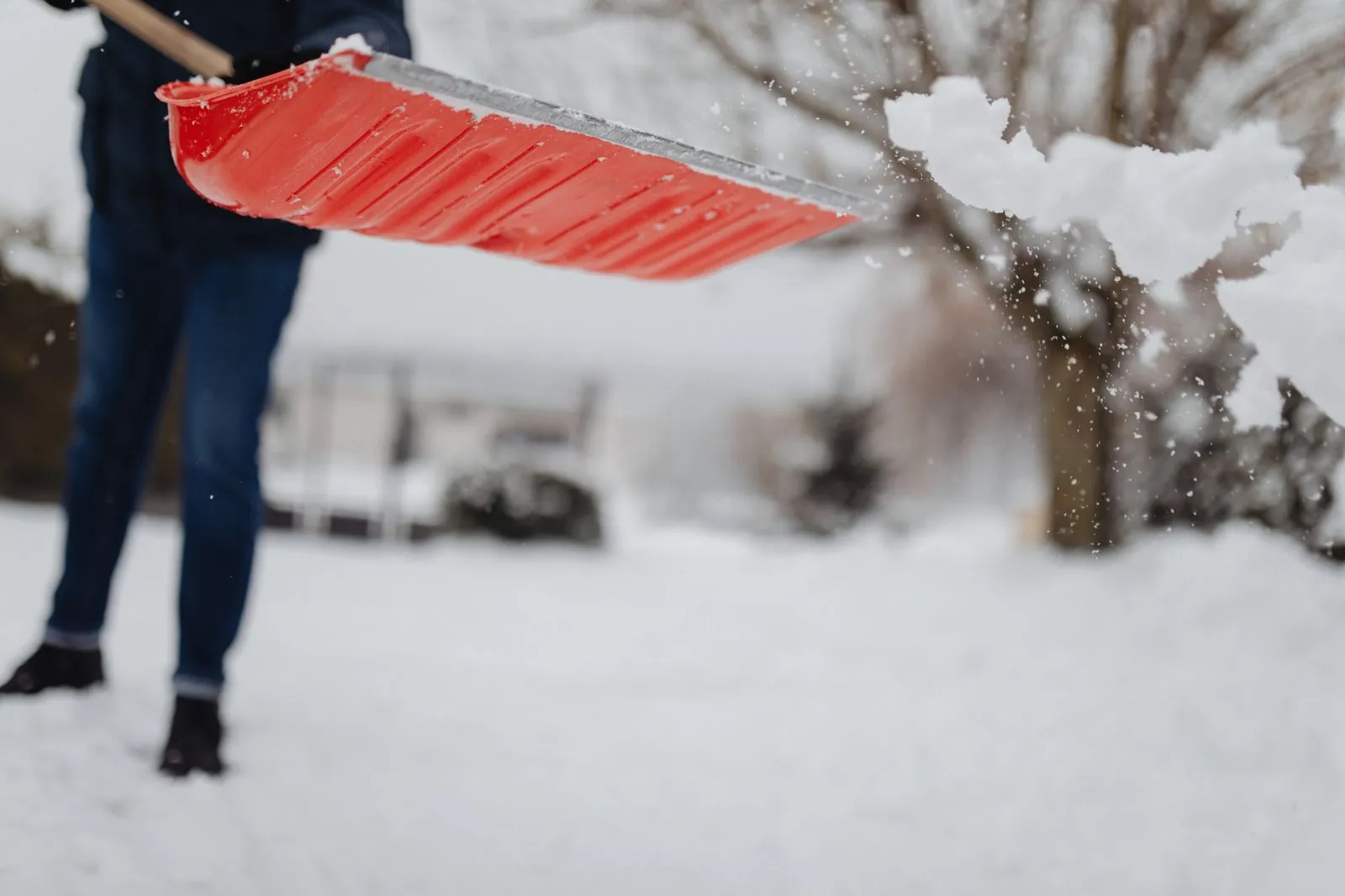 Person tossing snow from a red shovel while clearing a driveway