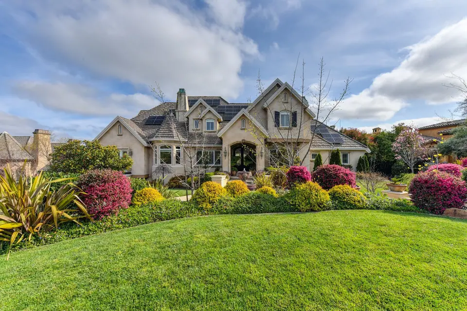 Large house with a green front lawn and flowering shrub beds