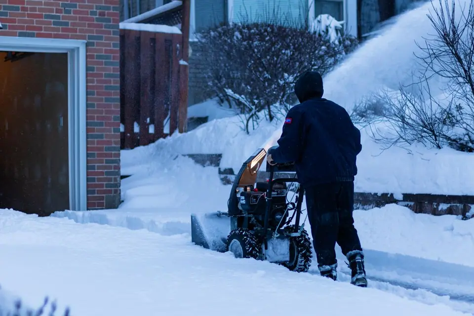 Person running a snowblower along a snow-covered driveway